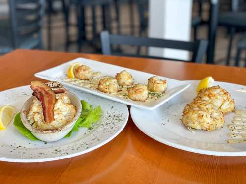 Three plates of crab cakes: one with bacon and lemon, two on a platter with sauce, all on a wooden table.