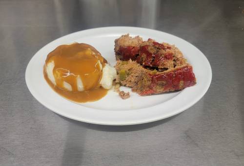 A plate with meatloaf, mashed potatoes topped with gravy, and a side of red sauce.