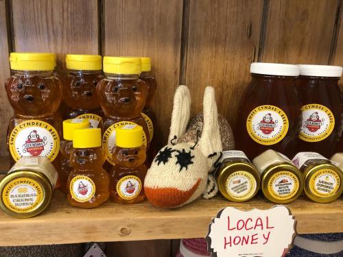A shelf displaying various honey jars, including bear-shaped bottles, alongside a knitted bunny and a sign for local honey.