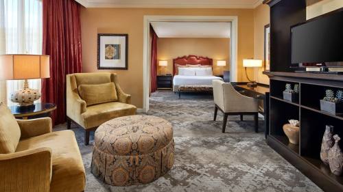A cozy hotel room featuring a sitting area with chairs, an ottoman, and a view of a bedroom in the background.