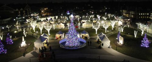 A festive night scene featuring a decorated Christmas tree surrounded by illuminated tents and trees in a park.