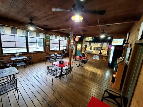 A cozy wooden interior of a restaurant with tables, chairs, and a counter area, featuring large windows and a warm atmosphere.