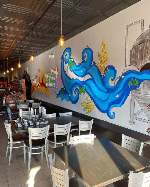 Colorful mural of waves and wheat on a restaurant wall, with tables and chairs in a cozy dining area.