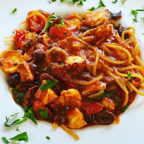 A plate of spaghetti with seafood, tomatoes, and herbs, garnished with fresh parsley.