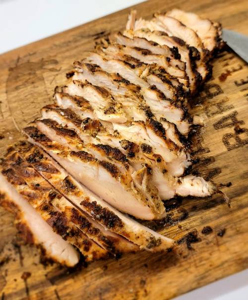 Sliced grilled chicken on a wooden cutting board, showcasing golden-brown, charred edges and juicy meat.