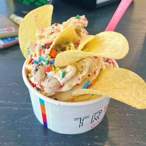 A cup of ice cream topped with colorful sprinkles and potato chips, with a pink spoon inserted.