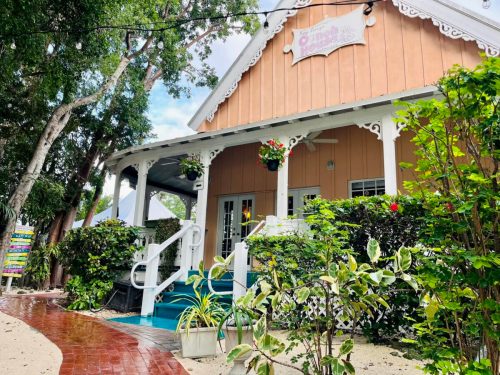 A charming building with a wooden facade, surrounded by greenery and flowers, featuring a welcoming porch.