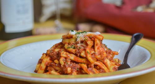 A plate of pasta with meat sauce, topped with grated cheese and parsley, served with a fork on a colorful table setting.