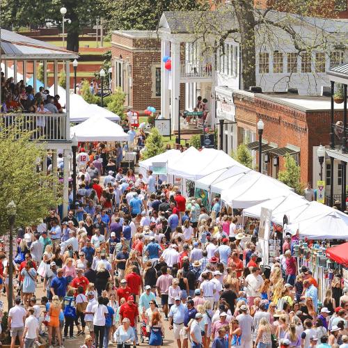 A bustling outdoor market scene with crowds of people browsing vendor tents and enjoying a sunny day.