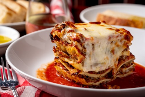 A delicious slice of lasagna with melted cheese, layered pasta, and marinara sauce, served on a white plate.