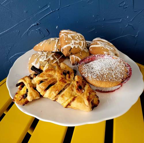 A white plate with assorted baked goods: iced cookies, a muffin, and a pastry, set against a blue wall.