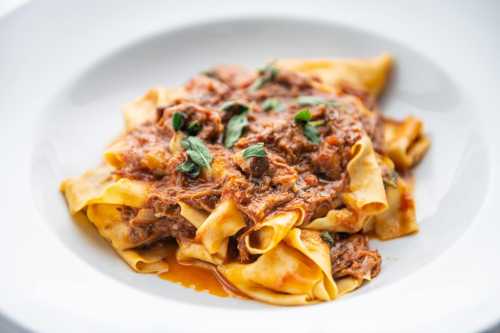 A plate of pappardelle pasta topped with a rich meat sauce and garnished with fresh herbs.