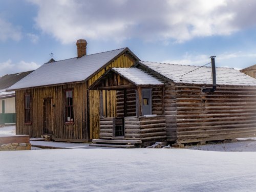 Two rustic wooden cabins covered in snow, with a cloudy sky in the background.