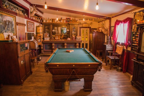 A vintage game room featuring a green pool table, wooden furniture, and rustic decor with warm lighting.