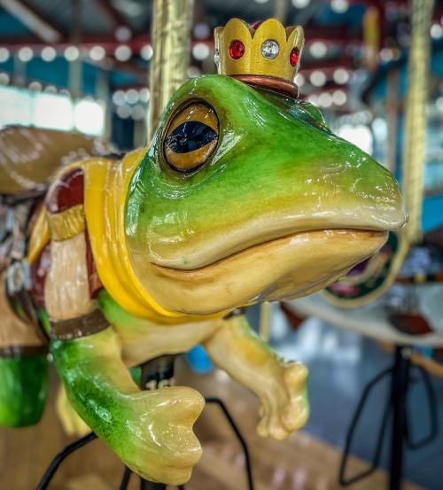 A whimsical green frog with a crown, featured on a colorful carousel.
