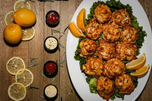 A platter of golden crab cakes on lettuce, garnished with lemon wedges and accompanied by dipping sauces.