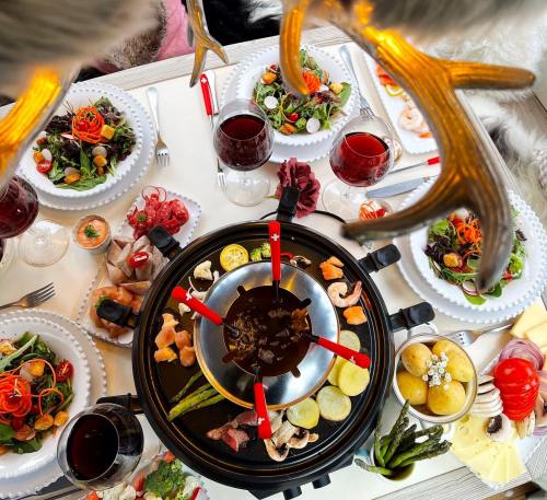 A festive table setting with a fondue pot, assorted meats, vegetables, salads, and drinks, surrounded by holiday decor.