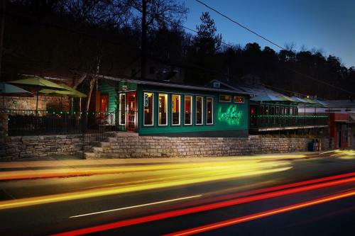 A green restaurant with outdoor seating, illuminated at dusk, with light trails from passing cars in the foreground.