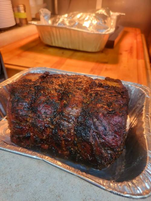A perfectly cooked, seasoned roast in a silver tray, with another covered dish in the background.