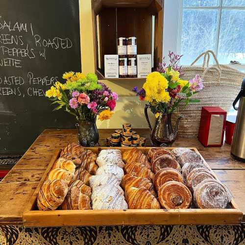 A wooden tray filled with assorted pastries, surrounded by colorful flower arrangements and a chalkboard menu.