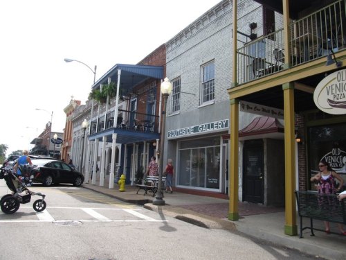 A street view of a charming town with shops, balconies, and pedestrians, showcasing a mix of architecture and activity.