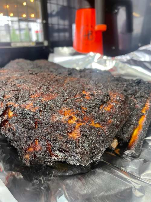 Close-up of a charred brisket resting on foil, showcasing a dark, crispy exterior.
