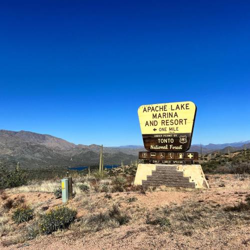 Sign for Apache Lake Marina and Resort, indicating it's one mile ahead, set against a clear blue sky and mountainous landscape.