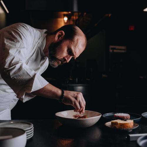 A chef carefully plating a dish in a modern kitchen, with various ingredients and plates on the counter.