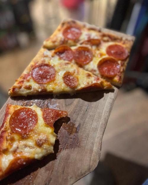 A wooden board holding slices of pepperoni pizza, with one slice partially eaten.