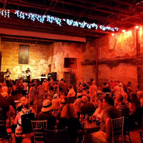 A lively indoor concert scene with a band performing on stage and a crowd enjoying the music in a rustic venue.