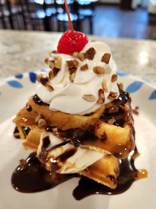 A delicious waffle topped with whipped cream, chocolate sauce, chopped nuts, and a cherry.
