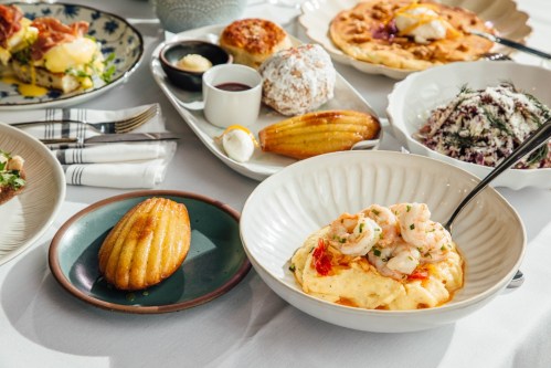 A table spread with various dishes, including shrimp and grits, pastries, and a colorful salad.
