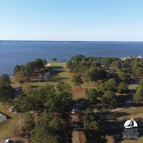 Aerial view of a serene lakeside park with trees and a calm water body in the background.