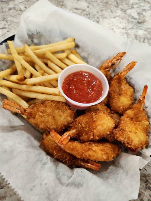 A basket of golden fried shrimp with a side of French fries and a small cup of dipping sauce.
