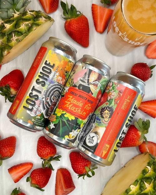 Three colorful beer cans from Lost Shoe Brewery surrounded by fresh strawberries and pineapple, with a glass of beer nearby.