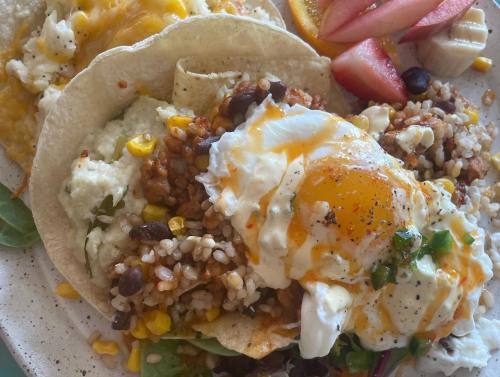 A plate of tacos topped with an egg, rice, beans, corn, and fresh fruit on the side.