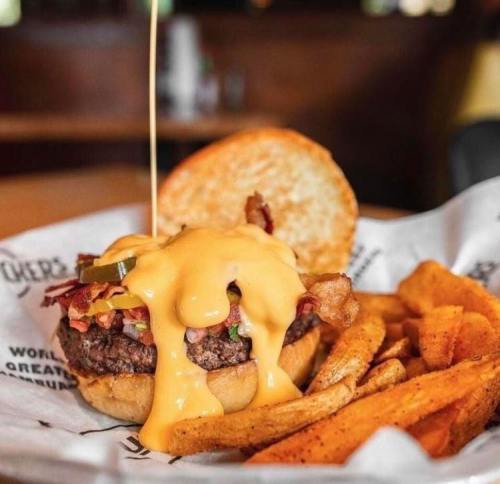 A juicy burger topped with melted cheese, bacon, and pickles, served with crispy fries on the side.