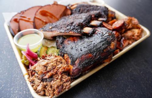 A platter of smoked meats including brisket, sausage, and pulled pork, served with pickles and sauce.