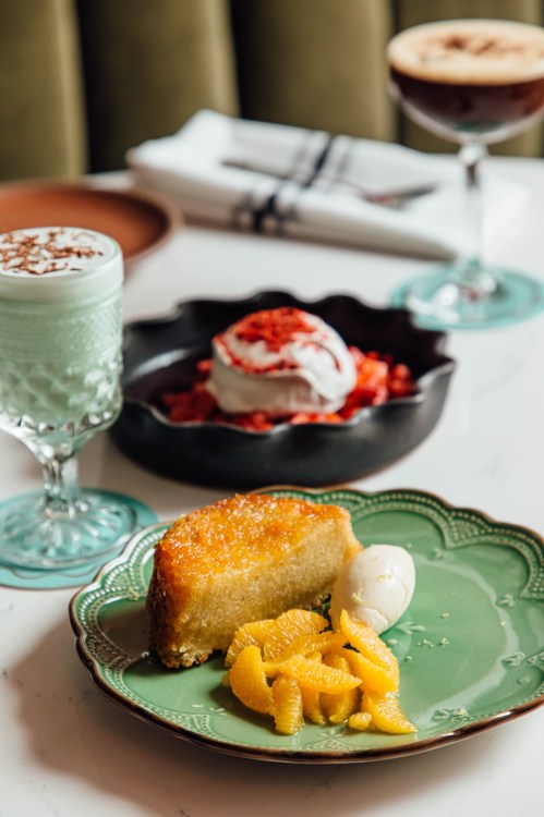 A plate with cake, orange slices, and ice cream, with desserts and drinks in the background on a marble table.