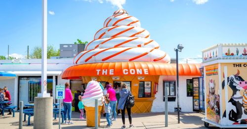 A colorful ice cream shop with a large cone-shaped roof and a pink ice cream statue outside, bustling with visitors.