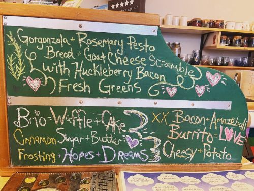 Chalkboard menu featuring creative dishes like Gorgonzola pesto bread and bacon burrito, with whimsical designs.