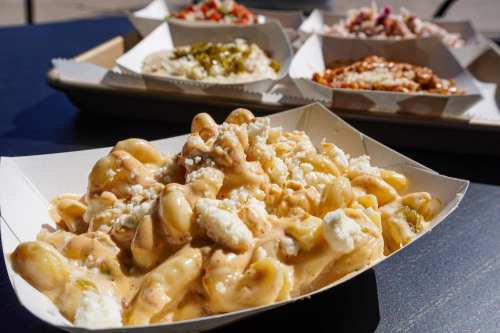 A serving of creamy macaroni topped with crumbled cheese, with other dishes blurred in the background.