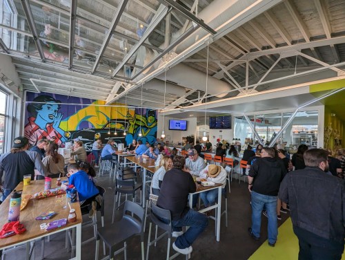 A busy restaurant interior with colorful murals, people dining, and a bright, modern atmosphere.