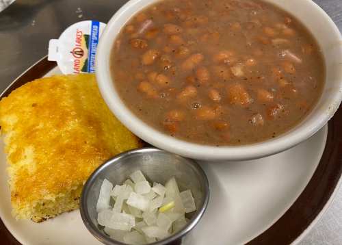 A bowl of pinto beans with cornbread and a side of diced onions on a plate.