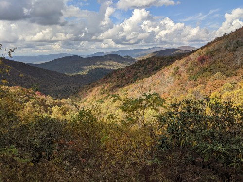A scenic view of rolling mountains covered in autumn foliage under a partly cloudy sky.
