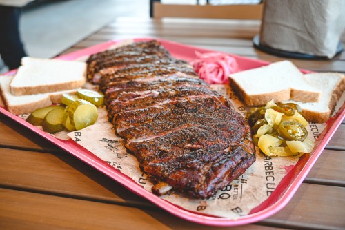 A tray of barbecue ribs with pickles, jalapeños, and slices of bread, served on butcher paper.