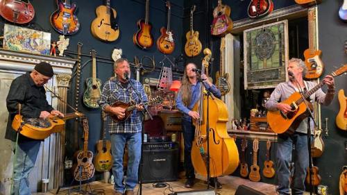 A group of four musicians perform on stage surrounded by various guitars and musical instruments.