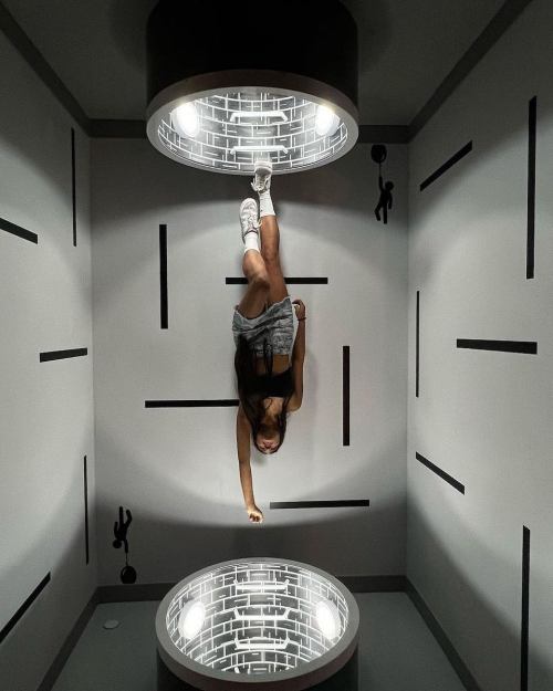 A person hangs upside down in a creatively designed room with two circular light fixtures and abstract wall patterns.