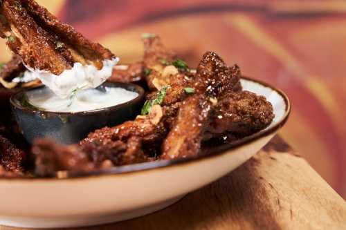 A plate of crispy chicken wings with a small bowl of dipping sauce, garnished with herbs.