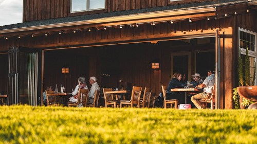 A cozy restaurant patio with diners enjoying their meals in warm evening light, surrounded by wooden architecture.
